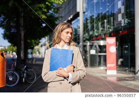 Work and corporate people. Confident businesswoman holding a blue folder with business documents, walking on street 96350857