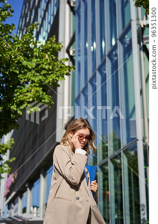 Portrait of confident saleswoman going to work, wearing sunglasses and suit. Businesswoman on her way to office, posing outdoors 96351300