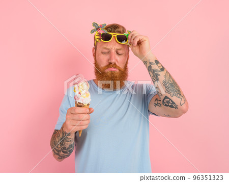 Thoughtful man with beard and tattoos eats a big icecream 96351323