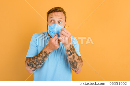 Afraid man with beard, tattoo and mask for covid-19 wants to smoke a cigarette 96351902