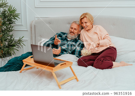 Husband and wife watch a film on the bed and eat popcorn 96351916
