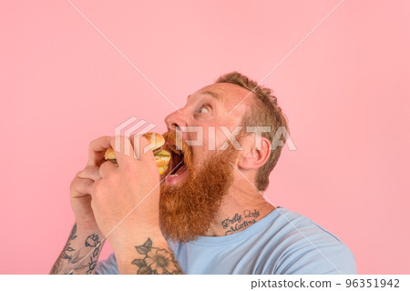 Hungry man with beard and tattoos eats a sandwitch with hamburger 96351942