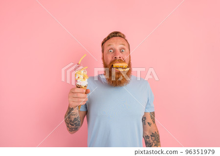 Amazed man with beard and tattoos is undecided if to eat an icecream or a sandwich with hamburger 96351979