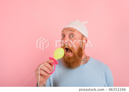 Man with beard and tattoos acts like a little newborn baby with pacifier in hand 96352266