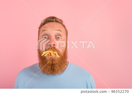 Hungry man with beard and tattoos eats a sandwitch with hamburger and potatoes Hungry man with beard and tattoos eats a sandwitch with hamburger and potatoes 96352270