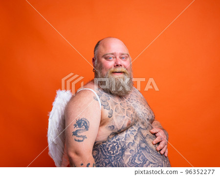 Fat happy man with beard ,tattoos and wings acts like an angel Fat happy man with beard ,tattoos and wings acts like an angel 96352277