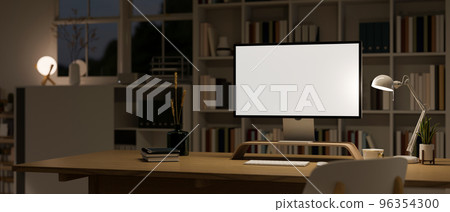Modern office at night with PC computer mockup on wood table over blurred bookshelves 96354300