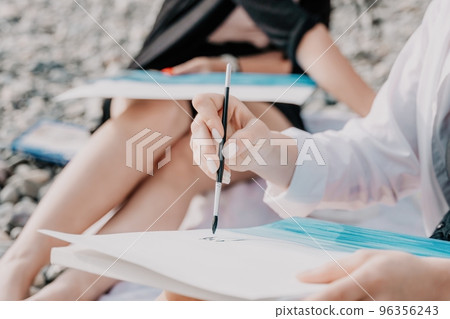 Unrecognizable woman's hands holding her own sea beach scenery watercolor painting. Amateur painter. Creative female artist drawing the picture at the beach. Art, creativity and inspiration concept. Unrecognizable woman's hands holding her own sea beach scenery watercolor painting. Amateur painter. Creative female artist drawing the picture at the beach. Art, creativity and inspiration concept. 96356243