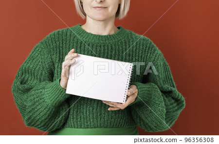 woman in a green sweater on a red background holds a notepad in her hands, a space for copying woman in a green sweater on a red background holds a notepad in her hands, a space for copying 96356308