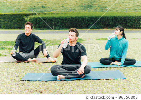 Man and woman drinking water and resting while doing yoga in the park Man and woman drinking water and resting while doing yoga in the park 96356808