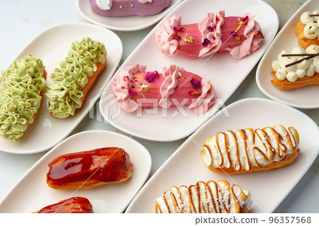 Set of colored eclairs with whipped cream on white plates 96357568