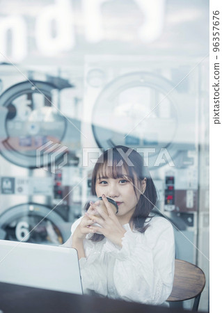在自助洗衣店咖啡廳工作時等待選擇完成的年輕女性 96357676