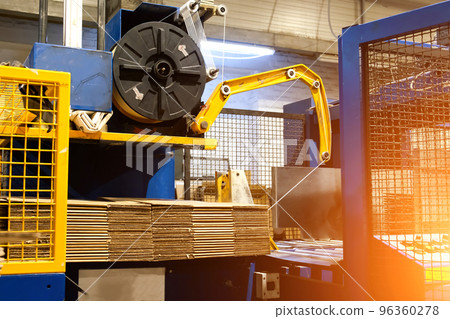 Ready-made cardboard boxes are moved in stacks along an automated packaging line. The strapping machine packs the stacks with thick white thread. Paper corrugated box factory. Ready-made cardboard boxes are moved in stacks along an automated packaging line. The strapping machine packs the stacks with thick white thread. Paper corrugated box factory. 96360278