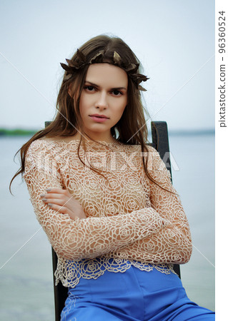 Calm fashion model in blue pants and lace blouse sitting on chair in a cloudy day on a beach Calm fashion model in blue pants and lace blouse sitting on chair in a cloudy day on a beach 96360524