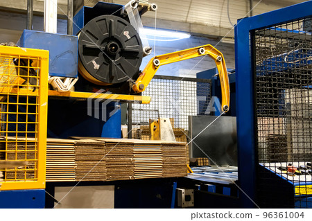 Ready-made cardboard boxes are moved in stacks along an automated packaging line. The strapping machine packs the stacks with thick white thread. Paper corrugated box factory. 96361004
