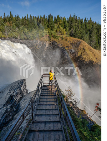 Girls standing on viewpoint bridge waterfall Tannforsen northern Sweden, rainbow in mist rapid flowing cascades of water Girls standing on viewpoint bridge waterfall Tannforsen northern Sweden, rainbow in mist rapid flowing cascades of water 96361867