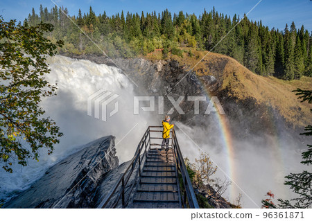 Girls standing on viewpoint bridge waterfall Tannforsen northern Sweden, rainbow in mist rapid flowing cascades of water Girls standing on viewpoint bridge waterfall Tannforsen northern Sweden, rainbow in mist rapid flowing cascades of water 96361871