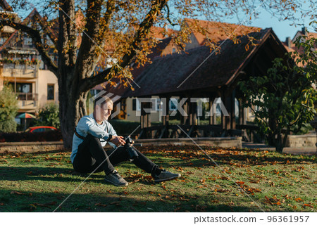 Professional Photographer Taking Picture Of Beautiful Autumn Park. Man Professional Photographer Sit With Camera And With Smartphone In Autumn Park. Retouched, Vibrant Colors, Brownish Tones. Professional Photographer Taking Picture Of Beautiful Autumn Park. Man Professional Photographer Sit With Camera And With Smartphone In Autumn Park. Retouched, Vibrant Colors, Brownish Tones. 96361957