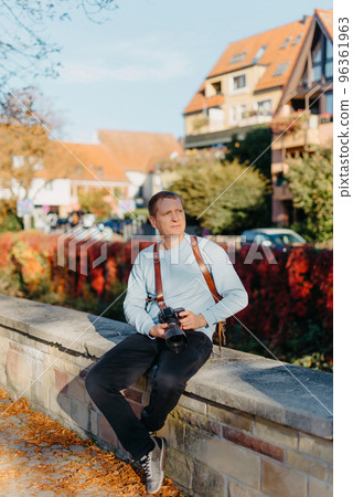 Man Sitting in Old European City And Holding Photo Camera. Contemporary Stylish Blogger And Photographer. Handsome man taking a selfie on a trip in Europe. Man Sitting in Old European City And Holding Photo Camera. Contemporary Stylish Blogger And Photographer. Handsome man taking a selfie on a trip in Europe. 96361963