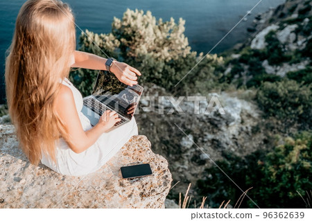 Digital nomad, Business woman working on laptop by the sea. Pretty lady typing on computer by the sea at sunset, makes a business transaction online from a distance. Freelance, remote work on vacation Digital nomad, Business woman working on laptop by the sea. Pretty lady typing on computer by the sea at sunset, makes a business transaction online from a distance. Freelance, remote work on vacation 96362639