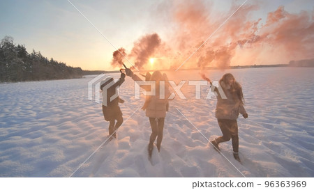 Girls friends run across the winter field with colored smoke. 96363969
