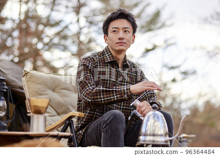 A young male camper resting by a firewood fire. A young male camper resting by a firewood fire. 96364484