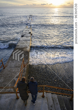 Two men on an old breakwater watching the sunset Two men on an old breakwater watching the sunset 96364530