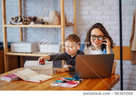 Young mother works with little boy. Business Woman talking on the phone and discussing work issues. Young mother works with little boy. Business Woman talking on the phone and discussing work issues. 96365008