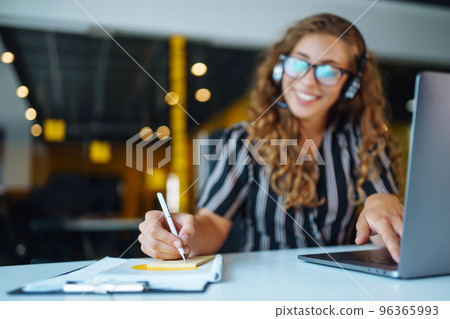 Meeting online. Young woman wearing headphones using laptop watching webinar or doing video chat. 96365993