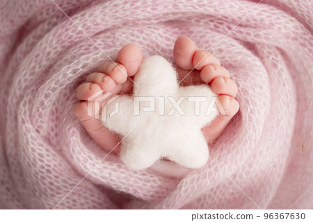 Knitted white star in the legs of a baby. Soft feet of a new born in a pink wool blanket. Close-up of toes, heels and feet of a newborn. Macro photography the tiny foot of a newborn baby.  96367630
