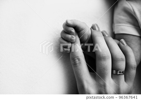 Close-up little hand of child and palm of mother and father. The newborn baby has a firm grip on the parent's finger after birth. A newborn holds on to mom's, dad's finger. Black and white photo. Close-up little hand of child and palm of mother and father. The newborn baby has a firm grip on the parent's finger after birth. A newborn holds on to mom's, dad's finger. Black and white photo. 96367641