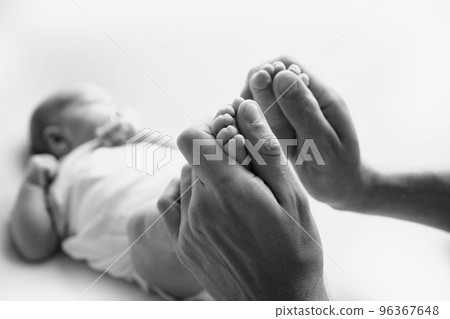 Legs, toes, feet and heels of a newborn. With the hands of parents, father, mother gently holds the child's legs. Macro photography, close-up. Black and white photo. High quality photo 96367648
