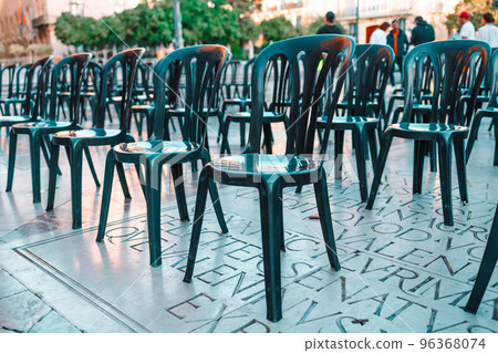 A lot of black empty chairs stand on the street. 96368074