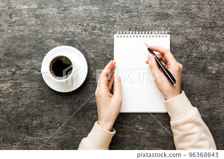 Woman hand with pencil writing on notebook and hold coffee cup. Woman working on office table with coffee 96368643
