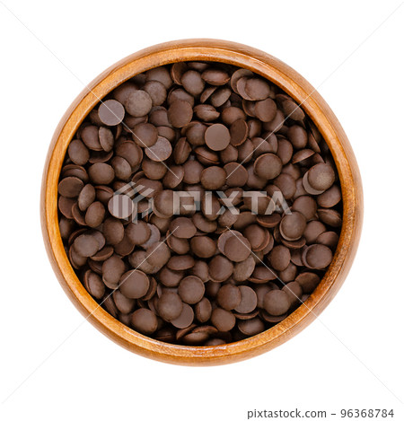 Bittersweet chocolate drops, couverture in a wooden bowl.  Chocolate coating mass in drop form, used in baking as topping or to add flavor to cookies, cakes and desserts. Close-up, from above. Photo. 96368784
