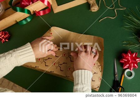 Top view of woman's hands wrapping a present for Christmas or New Year's events over green background. Boxing Day Top view of woman's hands wrapping a present for Christmas or New Year's events over green background. Boxing Day 96369804