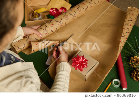 Overhead view of a woman cutting the wrapping paper for packing gift for Christmas, New Year or other celebration event Overhead view of a woman cutting the wrapping paper for packing gift for Christmas, New Year or other celebration event 96369810