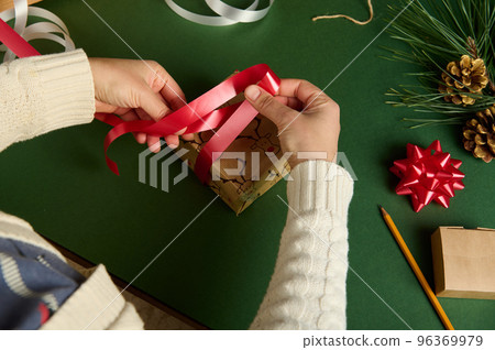 Top view woman tying up a present wrapped in a paper with deer pattern, using a red shiny ribbon. Diy gifts. Boxing Day. 96369979