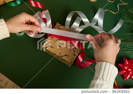 Top view woman holds red and white shiny ribbons over wrapping gift paper, packing presents for Christmas or New Year Top view woman holds red and white shiny ribbons over wrapping gift paper, packing presents for Christmas or New Year 96369982
