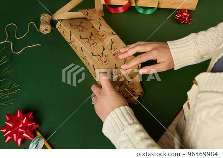 Top view woman wrapping a gift in a cute decorative paper with deer pattern over a green background. Copy ad space Top view woman wrapping a gift in a cute decorative paper with deer pattern over a green background. Copy ad space 96369984