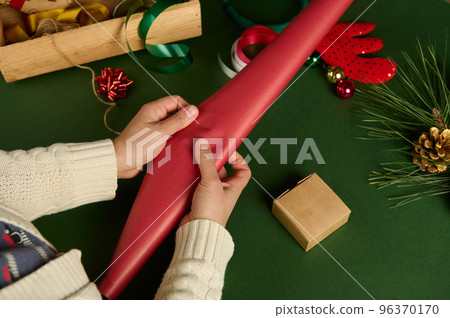 Top view woman's hand rolling out a red gift paper while, choosing wrapping decorative materials 96370170