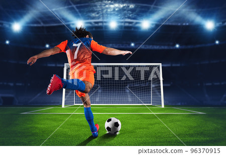 Soccer scene at night match with player in an orange and blue uniform kicking the penalty kick Soccer scene at night match with player in an orange and blue uniform kicking the penalty kick 96370915