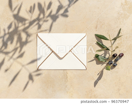 Blank envelope on concrete table with olive tree branches and hard shadows, wedding mockup 96370947