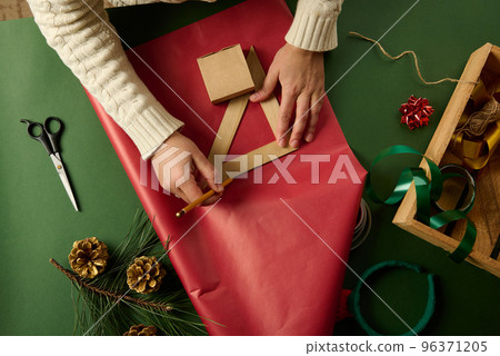 Woman using ruler to draw on gift paper, calculating amount of packaging materials needed to wrap Christmas present Woman using ruler to draw on gift paper, calculating amount of packaging materials needed to wrap Christmas present 96371205