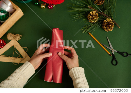 Close-up Top view woman packs a small present in red paper over a green background with wrapping materials. Diy presents 96372003