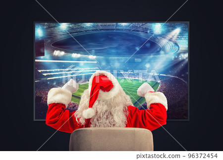Joyful Santa Claus, soccer fan, watches a game on television 96372454