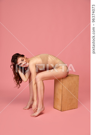 Portrait of young beautiful woman posing in beige underwear isolated over pink studio background. Tenderness and sensuality Portrait of young beautiful woman posing in beige underwear isolated over pink studio background. Tenderness and sensuality 96374073