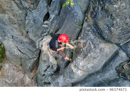 Young man climbing steep wall of rocky mountain. Male climber overcomes challenging route. Engaging in extreme sport concept. 96374671