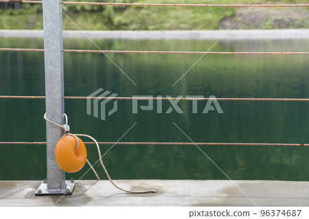 Yellow plastic buoy attached to a metal fence on the bank of a lake with green water. 96374687