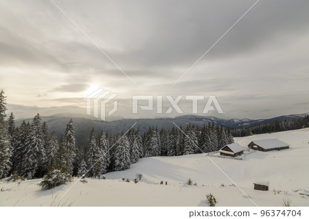 Winter mountain landscape. Old wooden houses on snowy clearing on background of mountain ridge, spruce forest and cloudy sky. Happy New Year and Merry Christmas card. 96374704